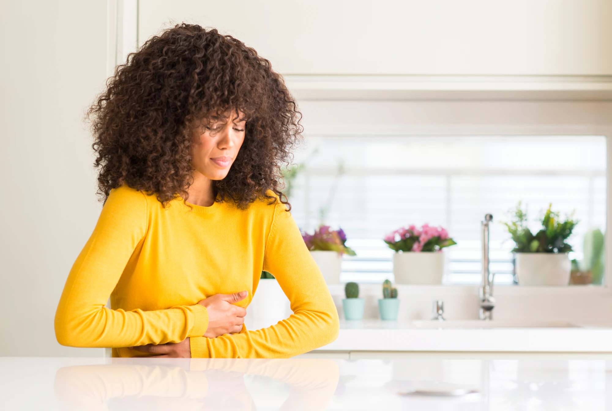 Woman sitting in her kitchen clutching her stomach from nausea.