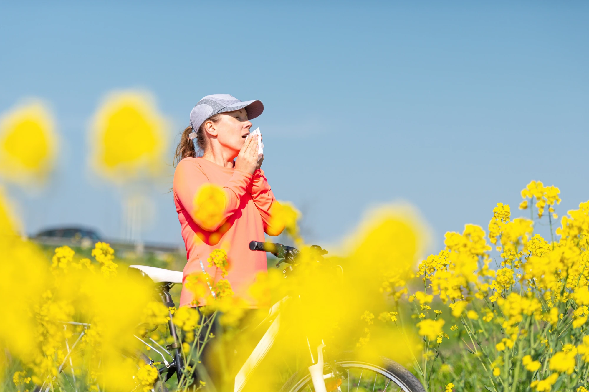 Woman sneezing while standing in a bunch of yellow pollen