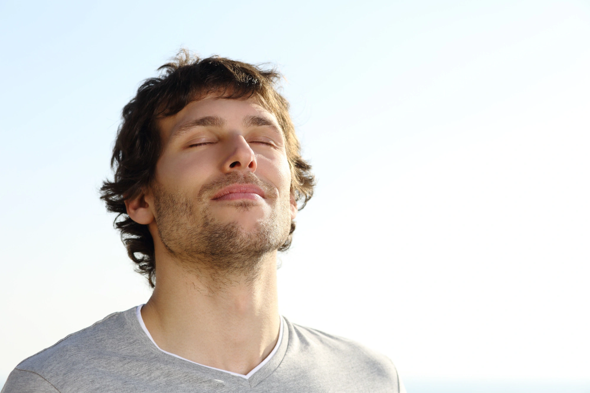 Man breathing in through his nose, relaxing with a blue sky behind him