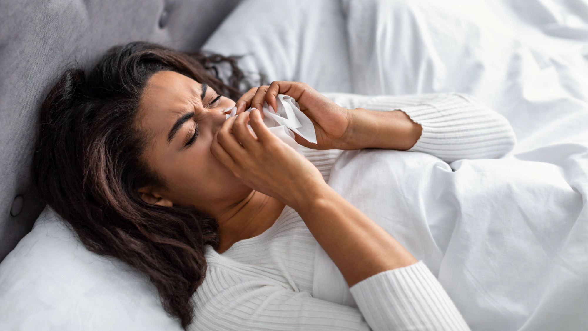 Black woman laying bed sick while blowing her nose