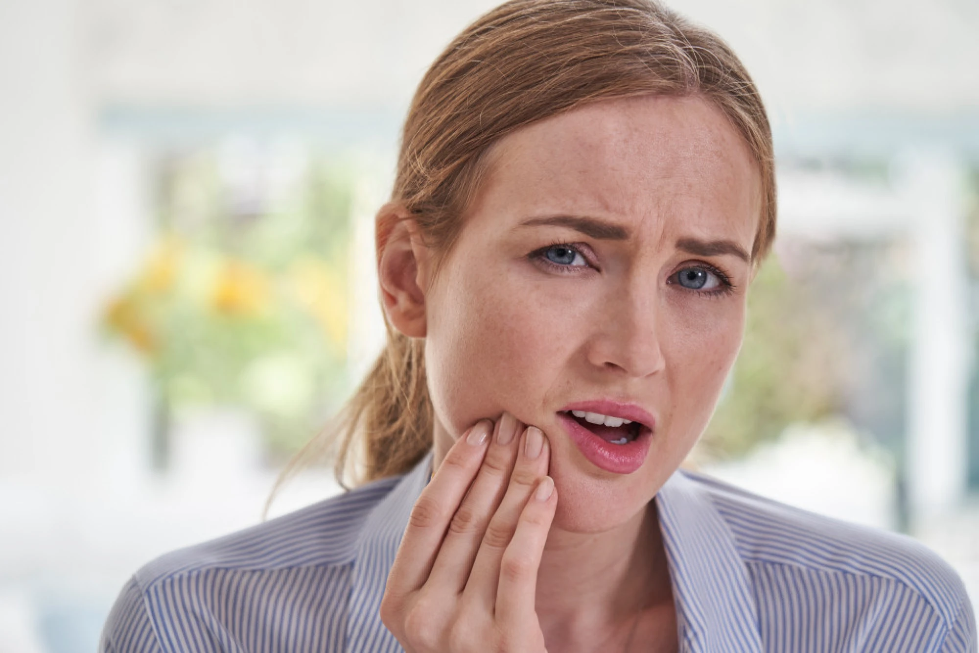 Young woman clutching her jaw in pain from TMJ