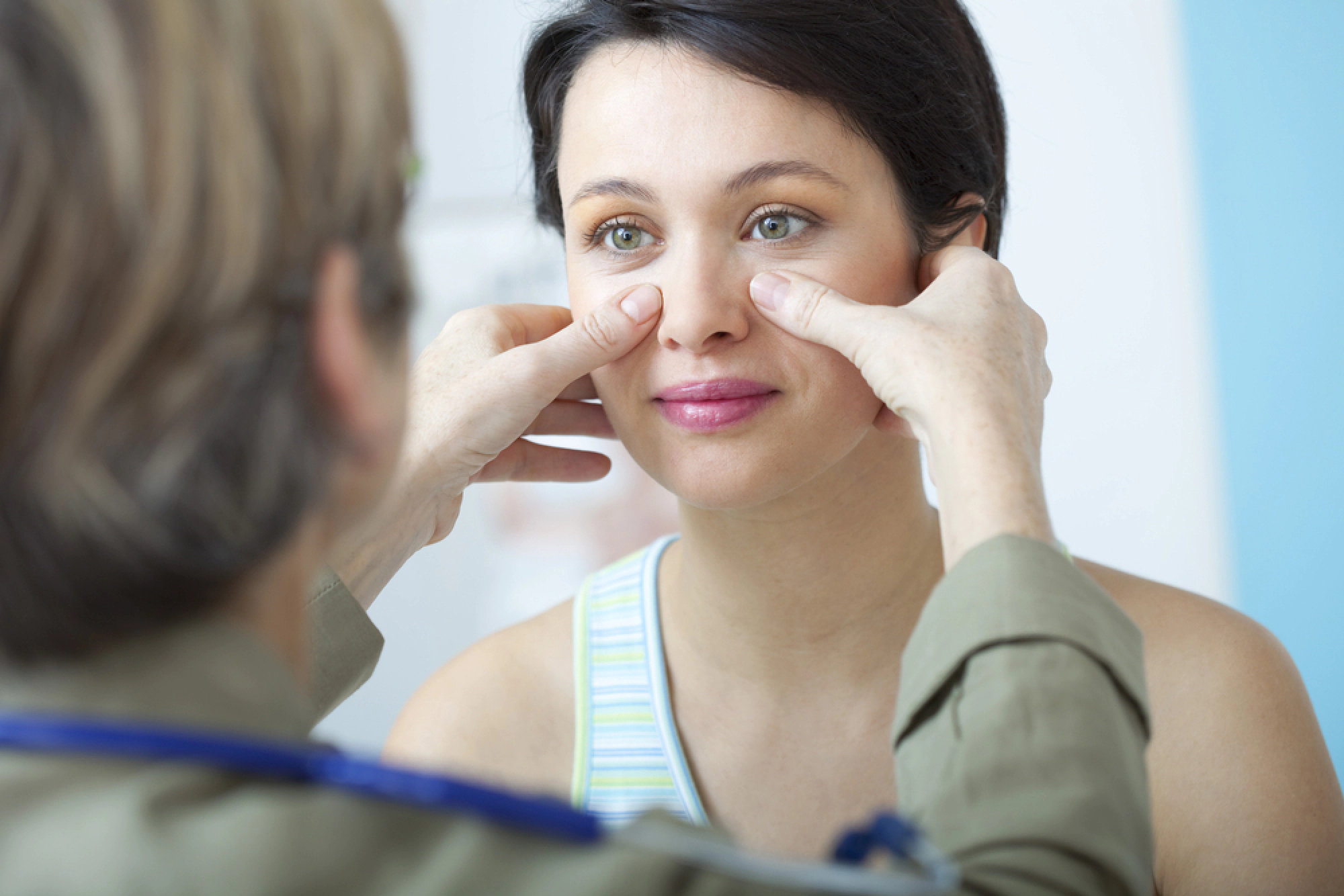 Doctor touching female patient’s face to check for sinus pressure.