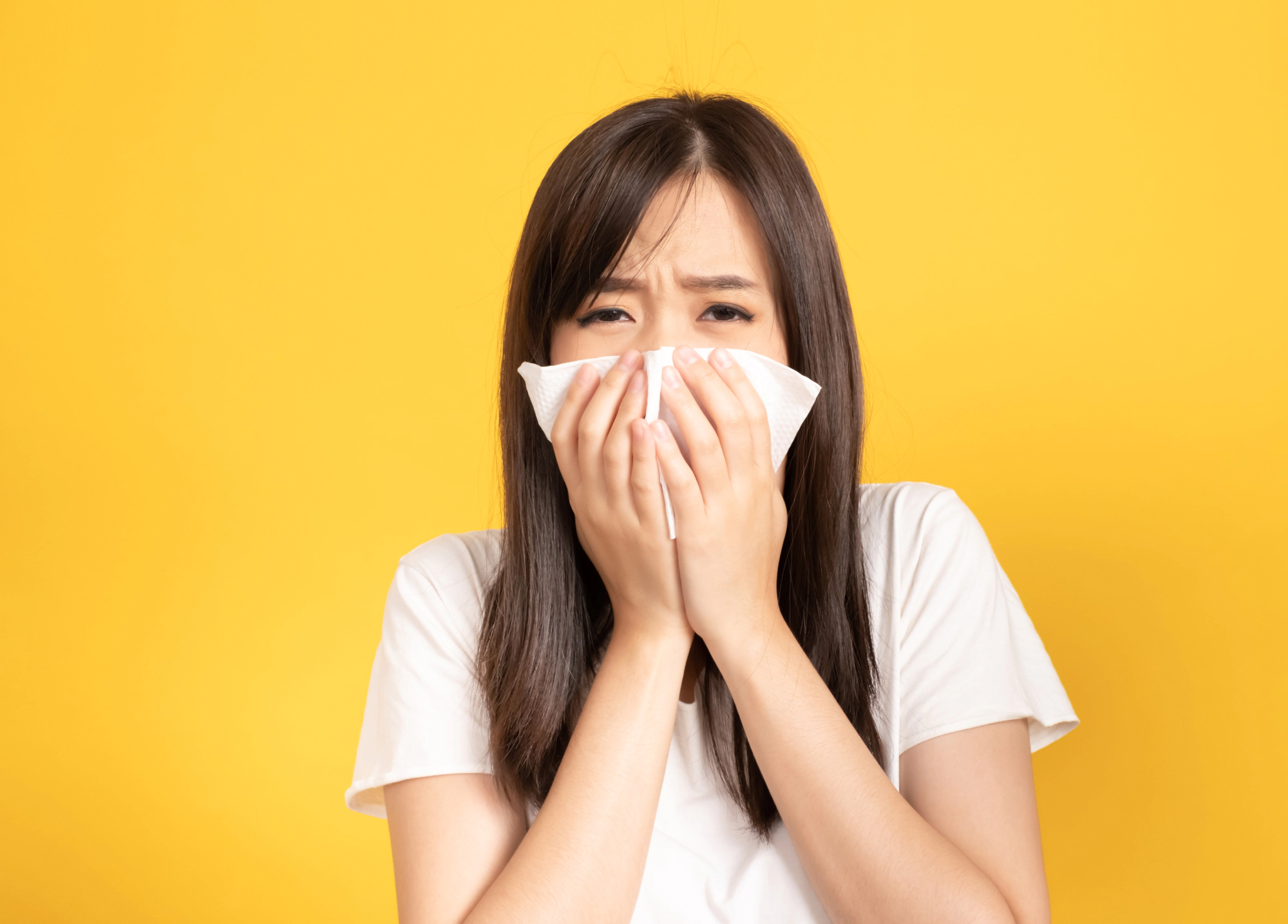 Woman blowing her nose against a yellow background.