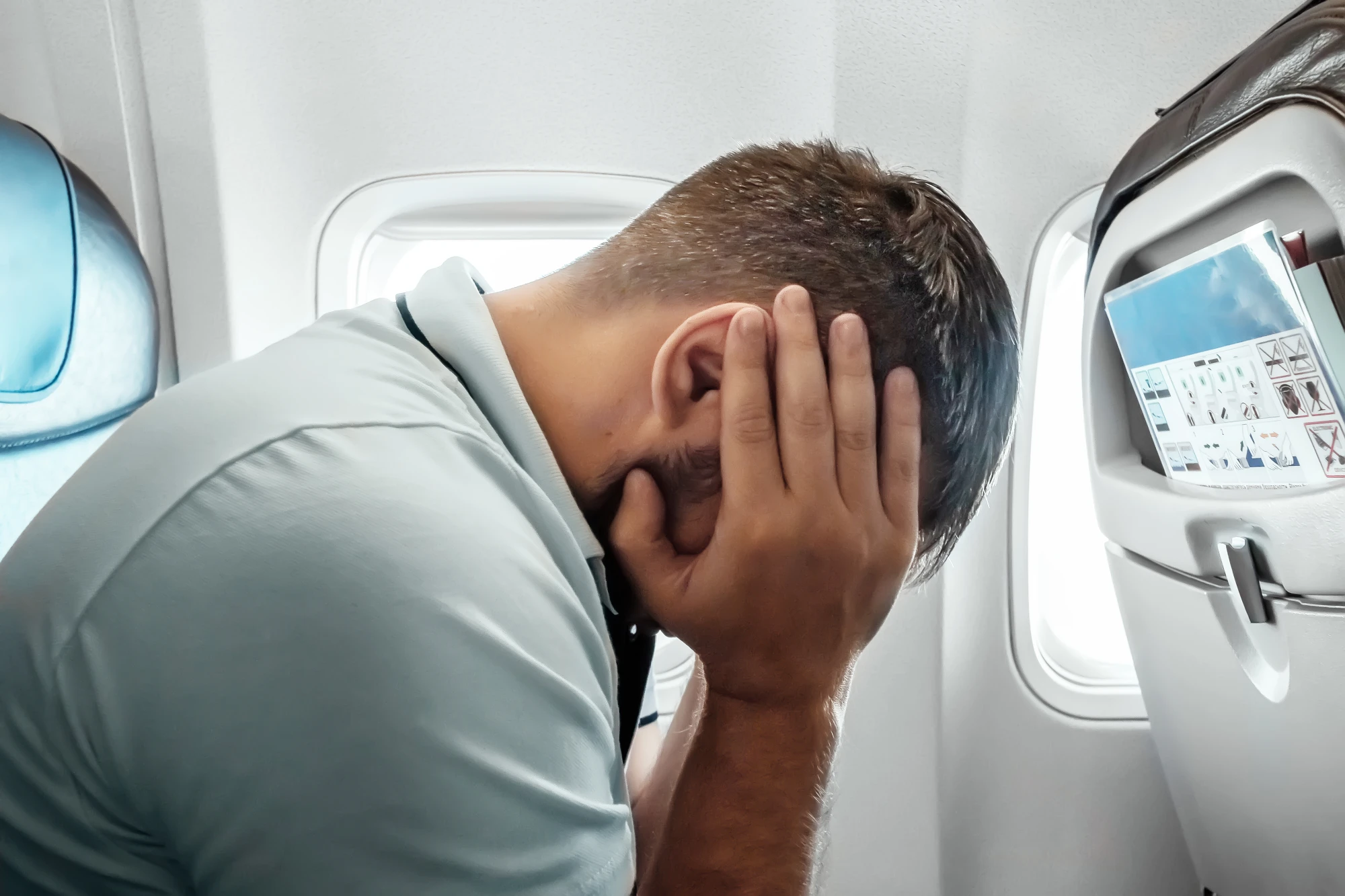 A man with his head in his hands, experiencing ear pressure while flying