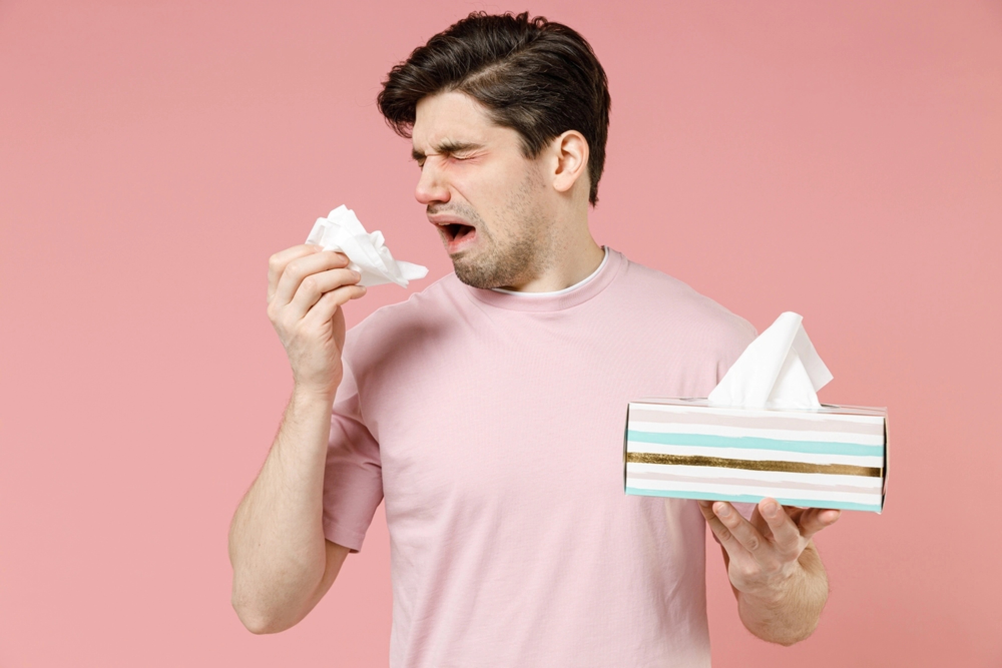 Sick man with tissues, red eyes, and a runny nose.