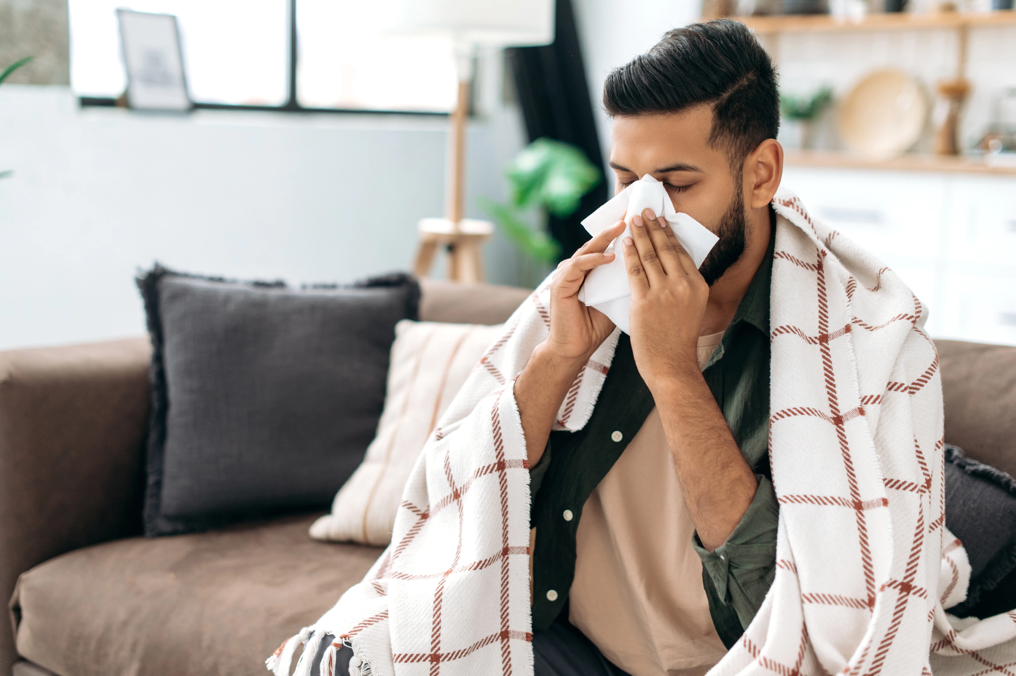 Man with a sinus infection blowing his nose on the couch