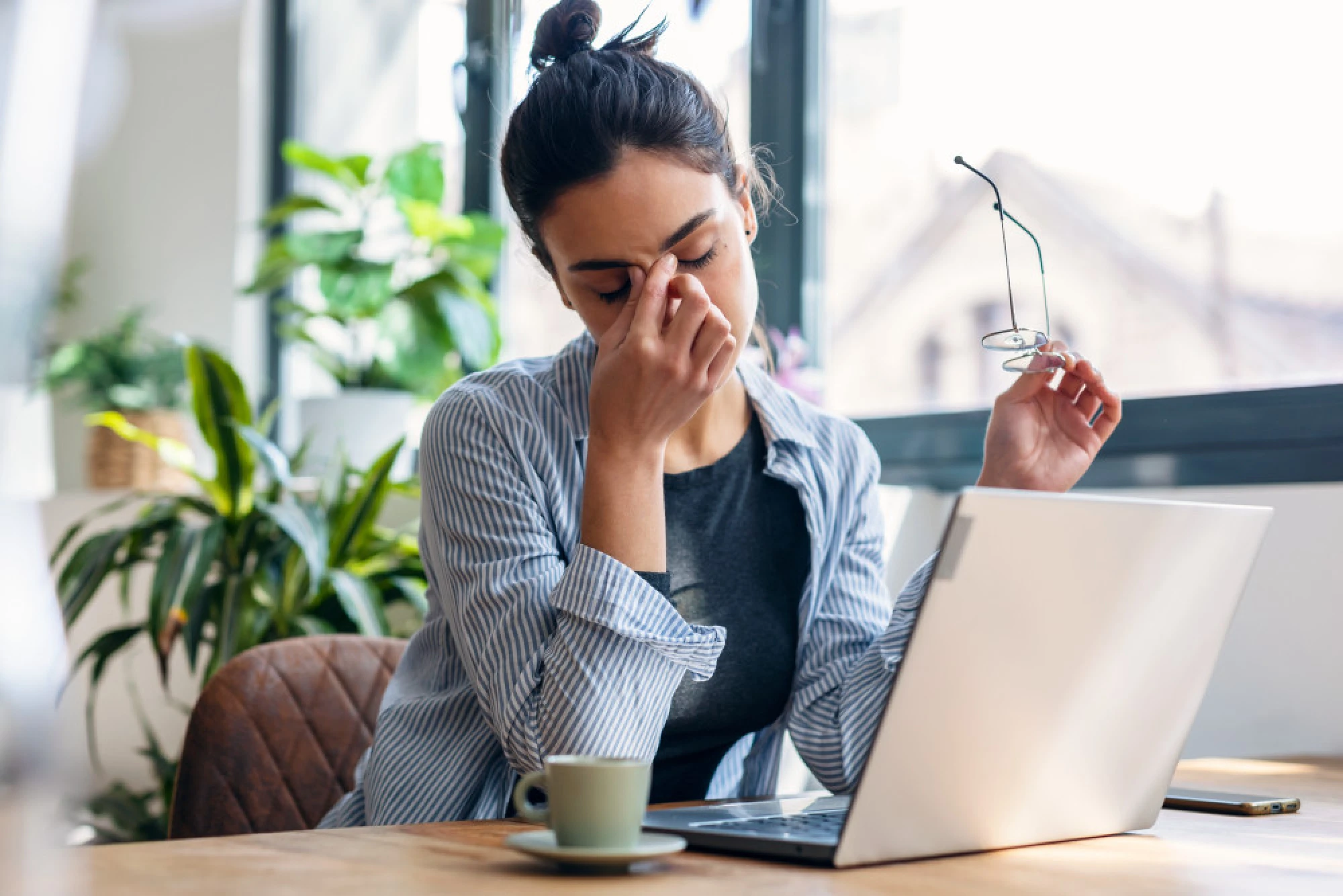 A woman sitting at her laptop, pinching the bridge of her nose due to sinus headache