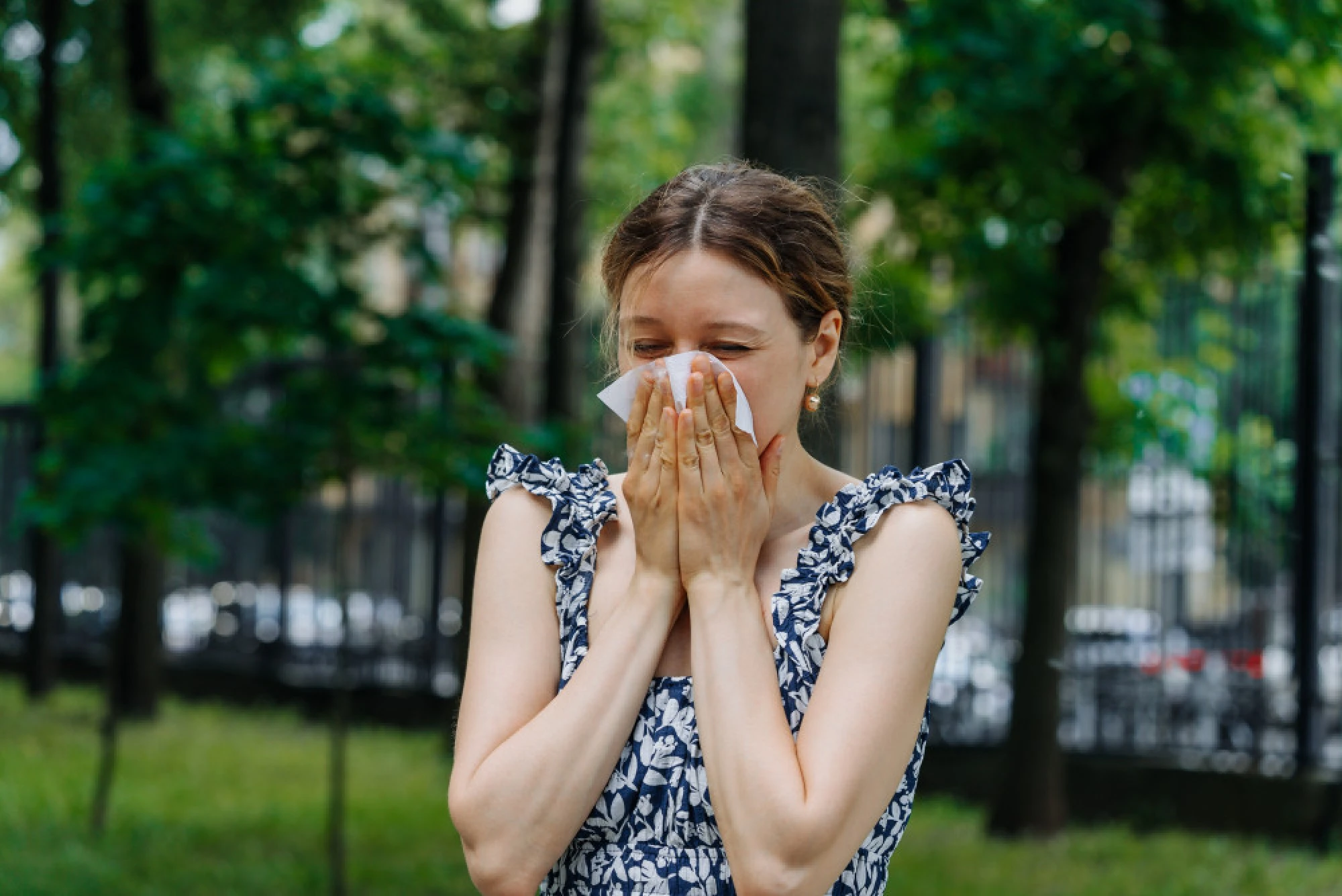 A woman blowing her nose from allergies in a Houston park
