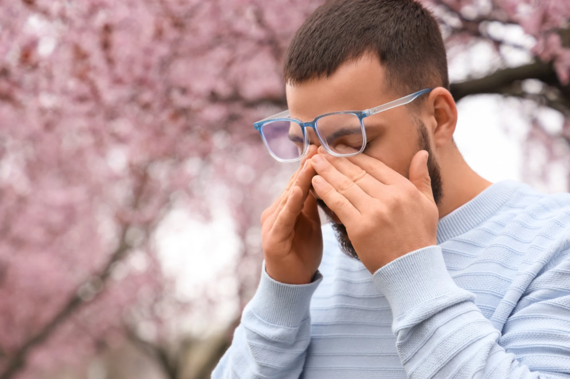 Man rubbing his itchy eyes next to a blossoming tree