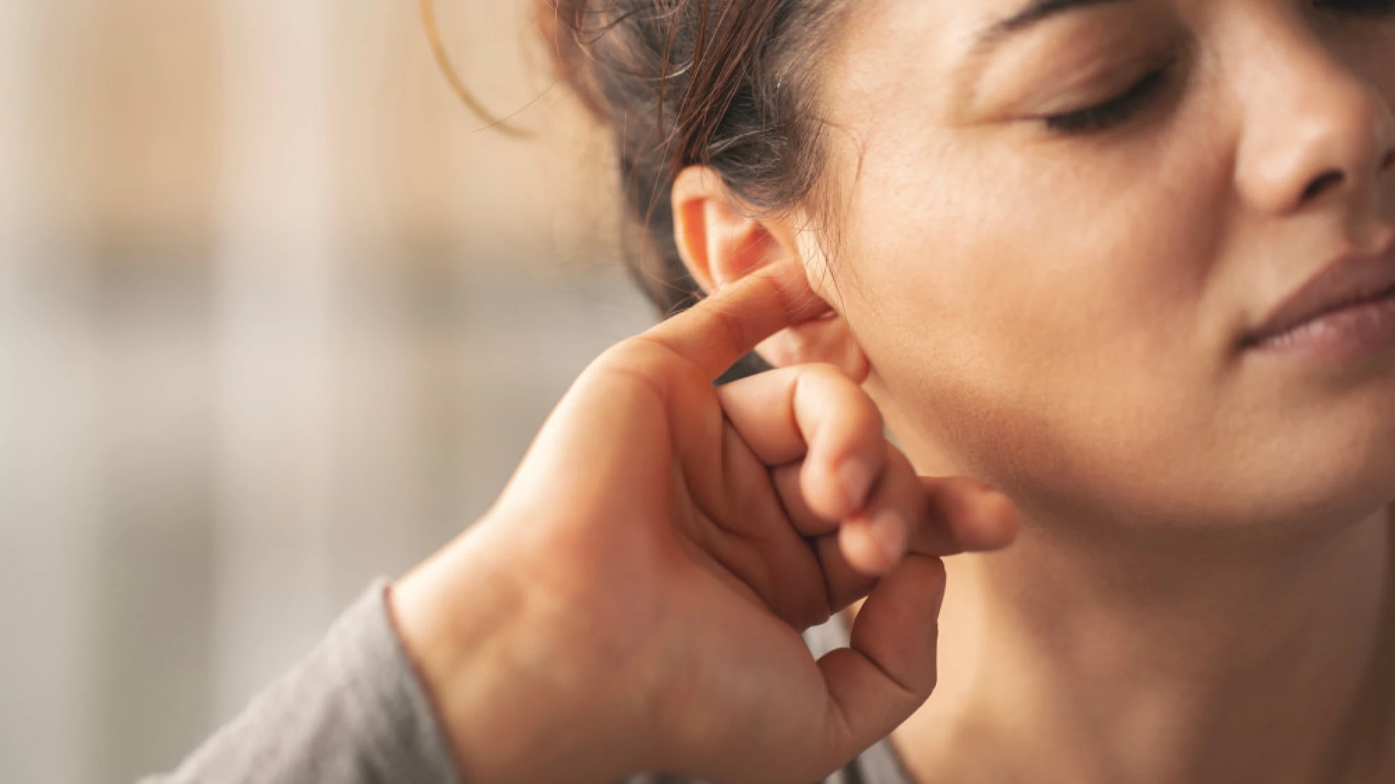 Woman with her finger in her ear, trying to unclog it